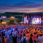 Vue panoramique du festival En Nord Beat au coucher du soleil, avec une foule dansant devant une grande scène illuminée.