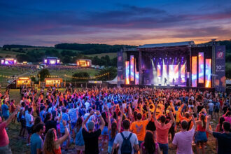 Vue panoramique du festival En Nord Beat au coucher du soleil, avec une foule dansant devant une grande scène illuminée.