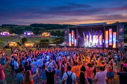 Vue panoramique du festival En Nord Beat au coucher du soleil, avec une foule dansant devant une grande scène illuminée.