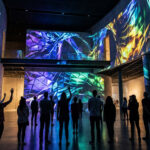 Groupe de personnes observant une projection de video mapping abstraite et colorée sur les murs d'un espace artistique.