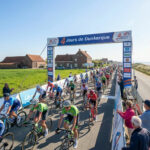 Un grand groupe de cyclistes professionnels passe sous une arche d'arrivée lors de la course des 4 Jours de Dunkerque.