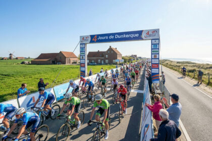 Un grand groupe de cyclistes professionnels passe sous une arche d'arrivée lors de la course des 4 Jours de Dunkerque.