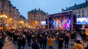 Une foule dense danse devant une grande scène de concert illuminée sur la Grand-Place de Lille à la tombée de la nuit.