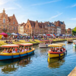 Vue ensoleillée du canal de Lille avec des bateaux colorés, des cyclistes et des gens se relaxant sur les berges.