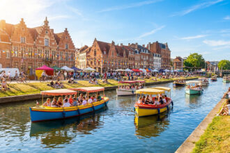 Vue ensoleillée du canal de Lille avec des bateaux colorés, des cyclistes et des gens se relaxant sur les berges.