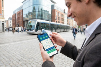 Un jeune homme tient un smartphone affichant l'application Ilevia devant un tramway à Lille.