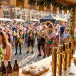 Un barman sert de la bière à la Braderie de Lille avec des musiciens en costumes traditionnels en arrière-plan.