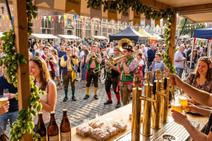 Un barman sert de la bière à la Braderie de Lille avec des musiciens en costumes traditionnels en arrière-plan.
